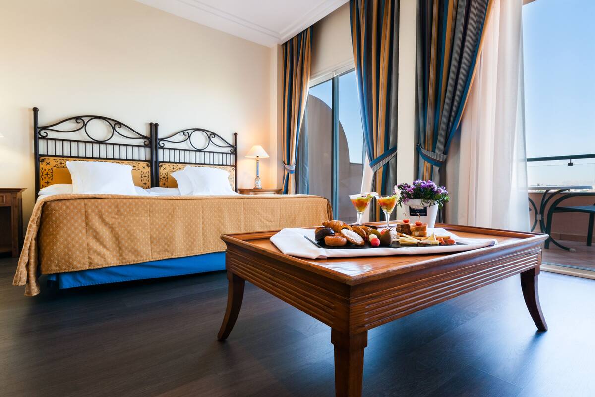 Una habitación de hotel con cama, una mesa de comedor con desayuno y vistas al exterior.