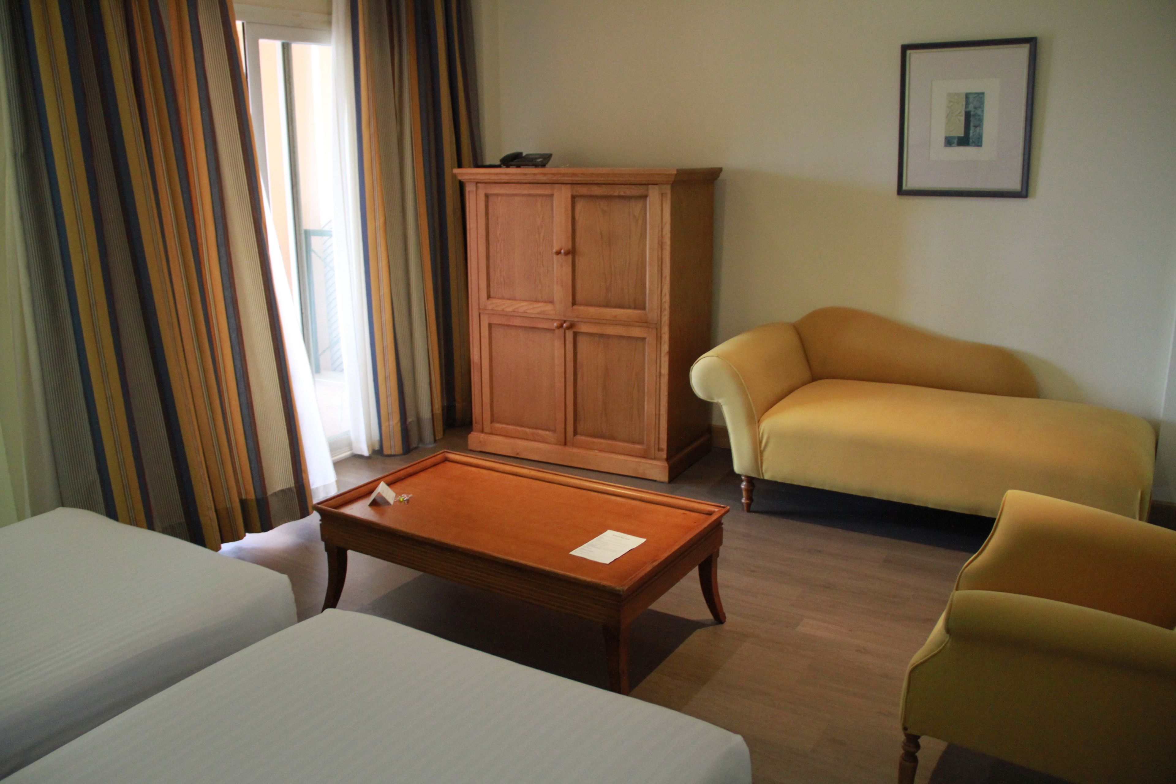 Ein Hotelzimmer mit zwei Betten, einem Holfachschrank, einem gelben Sessel und einem gerahmten Bild an der Wand.