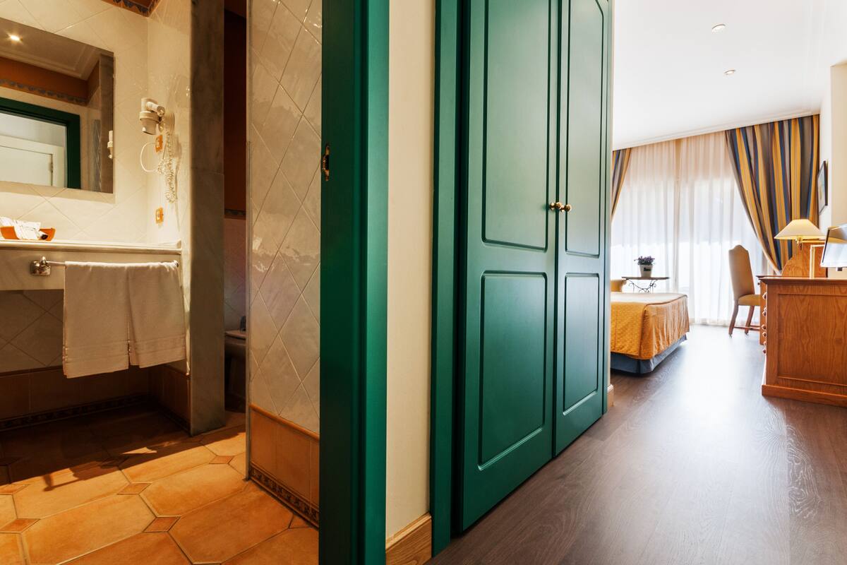 Habitación de hotel con baño, puerta verde, zona de comedor y escritorio de madera.