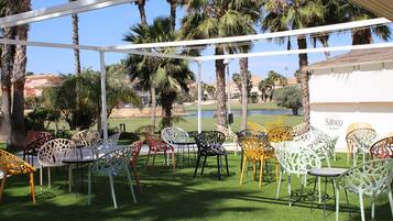 Een terras met verschillende stoelen en tafels, omringd door palmbomen en uitzicht op een golfbaan.