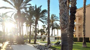 A sunlit outdoor area with palm trees, lounge chairs, and a paved walkway. - Hotel Alicante Golf (Alicante)