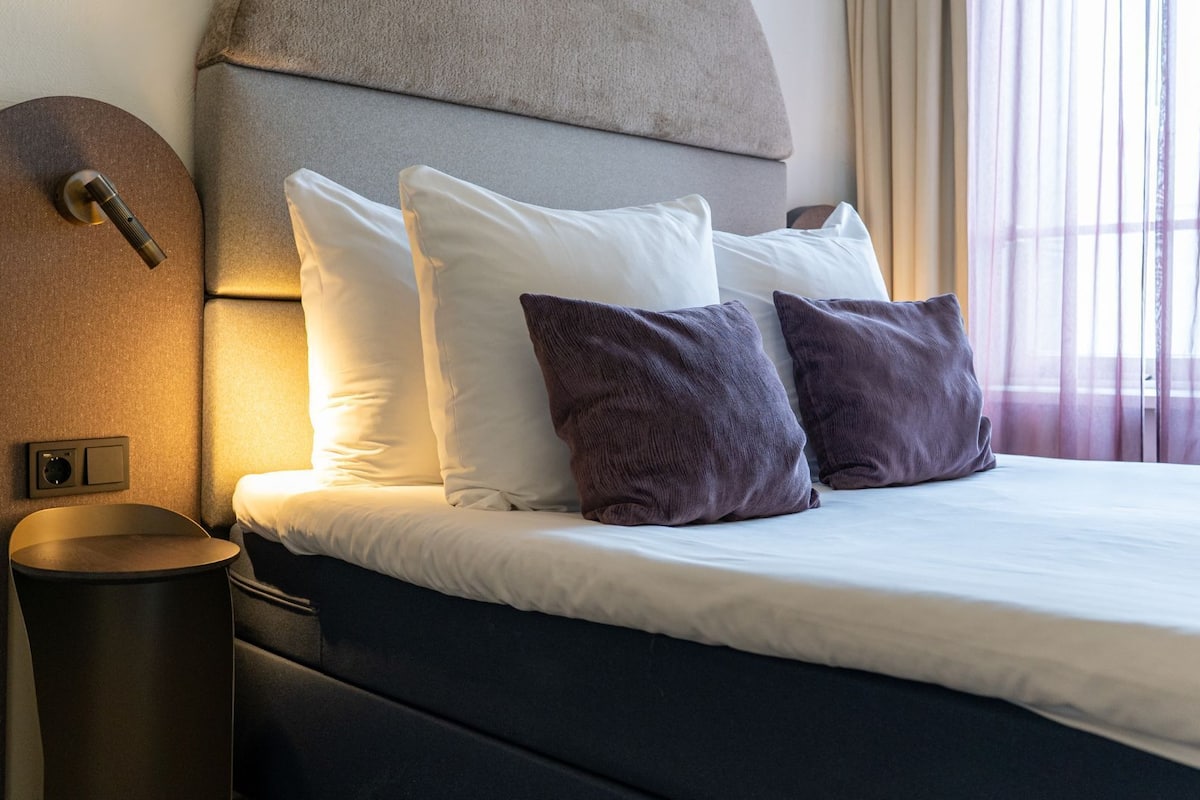 Une chambre d’hôtel avec un lit, des oreillers, une tête de lit et une table de chevet.