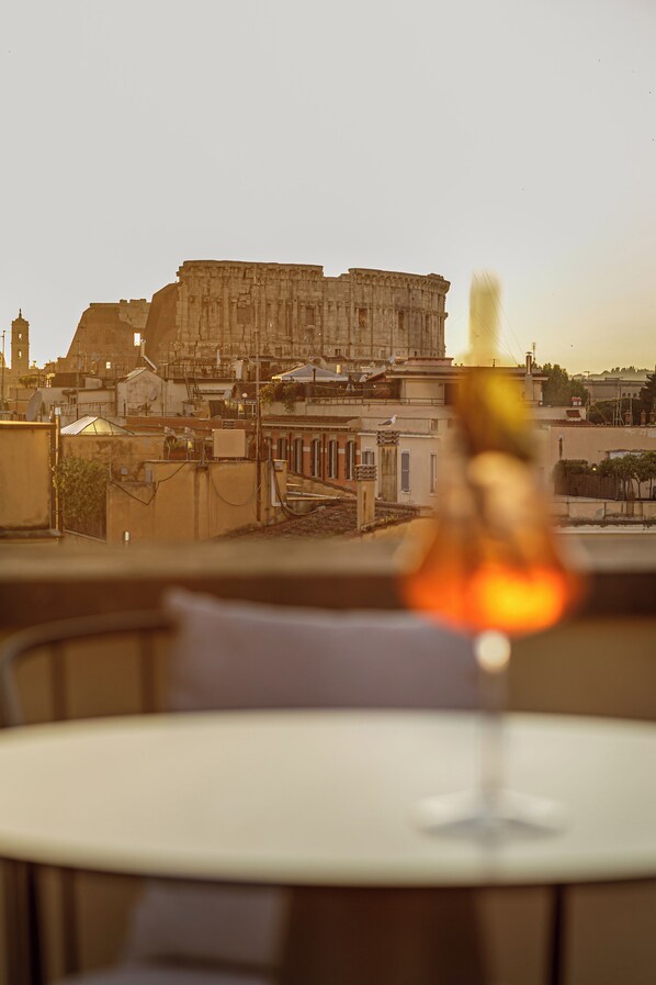 A table with a glass of wine, a chair, and a view of a large building in the background.
