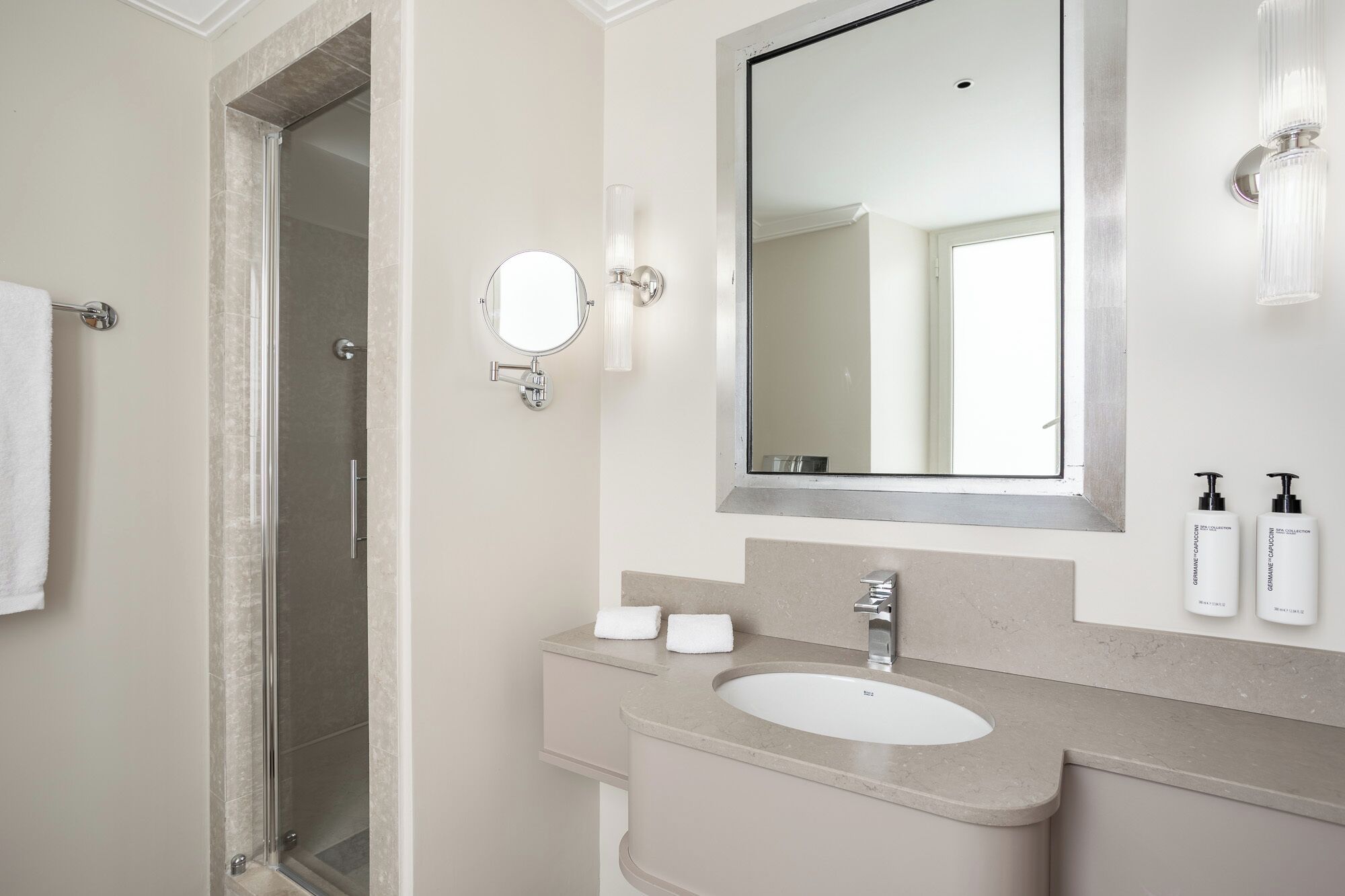 Een moderne badkamer met een glazen douchecabine, een grote spiegel, een wastafel en toiletartikelen op het aanrecht.