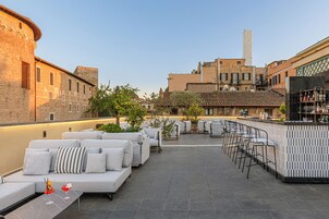 An outdoor seating area with sofas and chairs, a bar, and a view of historic buildings.