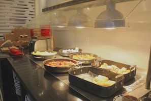 Buffet com diversos pratos, incluindo gratinados, saladas e pão.
