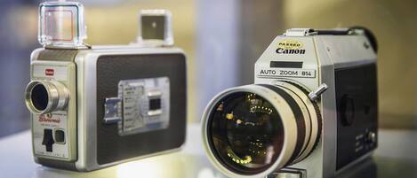 Two vintage cameras, one with a viewfinder and the other with an auto-zoom feature, displayed on a reflective surface.