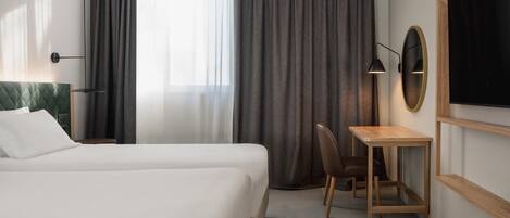 A hotel room with a bed, a desk, a chair, a lamp, and a TV.