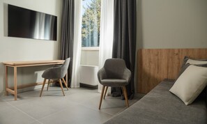 Una camera moderna con una scrivania in legno, due poltrone grigie, un letto con biancheria da letto grigia e un'ampia finestra con tende.