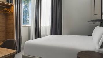 A hotel room with a bed, a desk, a chair, and a small table.