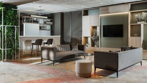 A modern living area with a sofa, ottoman, and bar area with wine bottles. - Hilton Garden Inn Bologna North (Granarolo dell'Emilia)