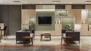 A modern lounge area with sofas, a coffee table, and a TV mounted on the wall. - Hilton Garden Inn Bologna North (Granarolo dell'Emilia)