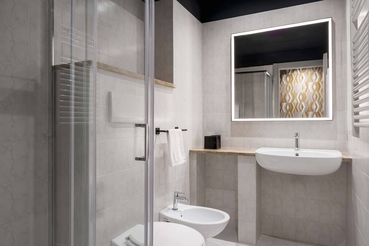 A modern bathroom with a glass-enclosed shower, a toilet, a bidet, and a sink with a mirror above.