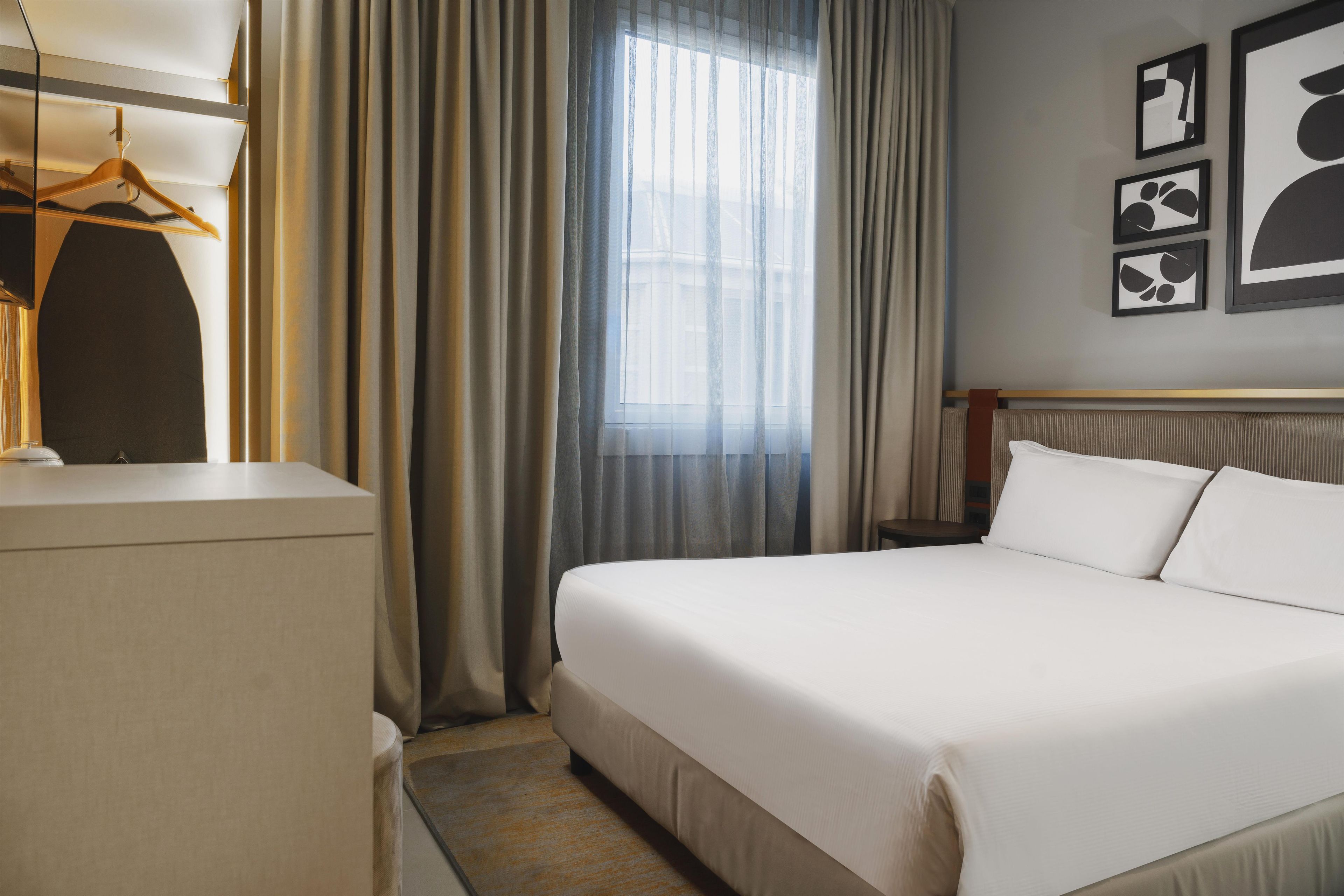 A hotel room with a bed, a desk, a chair, and a window with curtains.