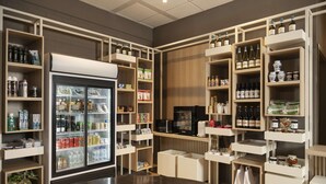A well-organized retail space with shelves stocked with various products, a refrigerator with beverages, and a coffee machine. - Hilton Garden Inn Bologna North (Granarolo dell'Emilia)