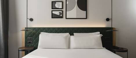 A neatly made bed with a green headboard, two bedside tables, and framed artwork on the wall.