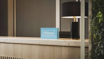 A reception desk with a 'Hilton Honors' sign, a black lamp, and a plant.