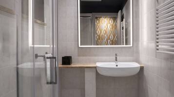 A modern bathroom with a glass shower enclosure, a white sink, and a mirror with a geometric pattern.