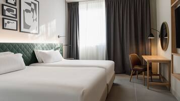 Habitación de hotel con dos camas, un escritorio, una silla, un televisor y obras de arte en la pared.
