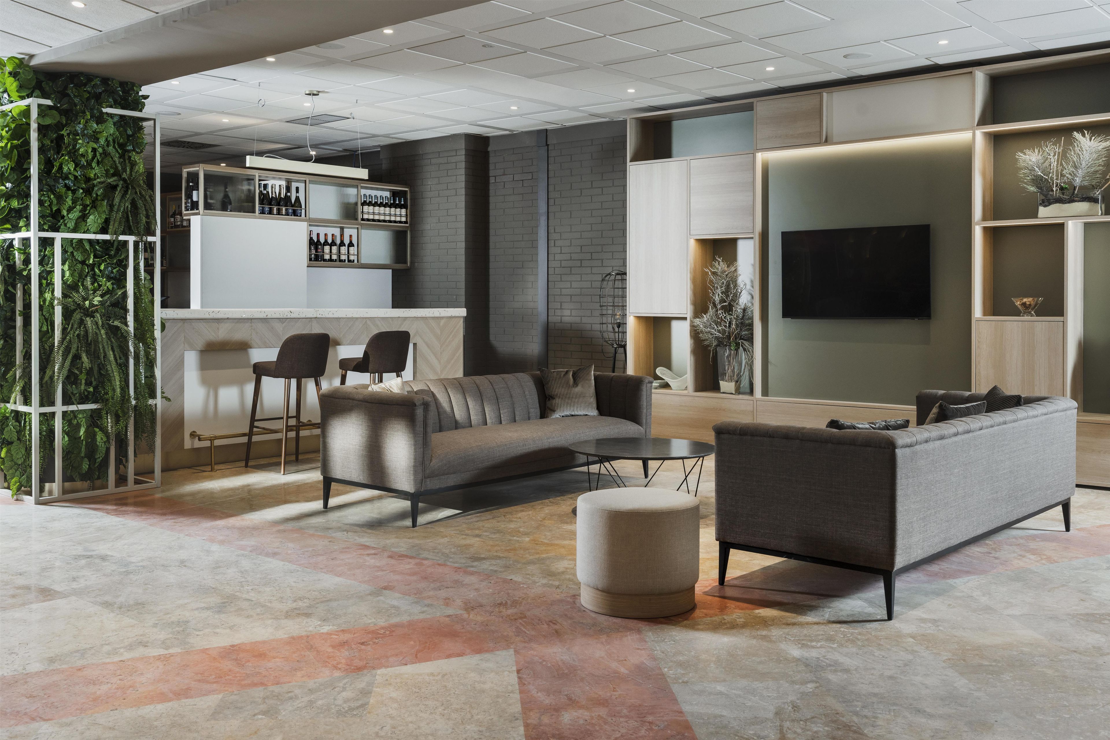 Una sala de estar moderna con un sofá, un reposapiés y una mesa de centro. Cuenta con una zona de bar con taburetes y un televisor montado en la pared.