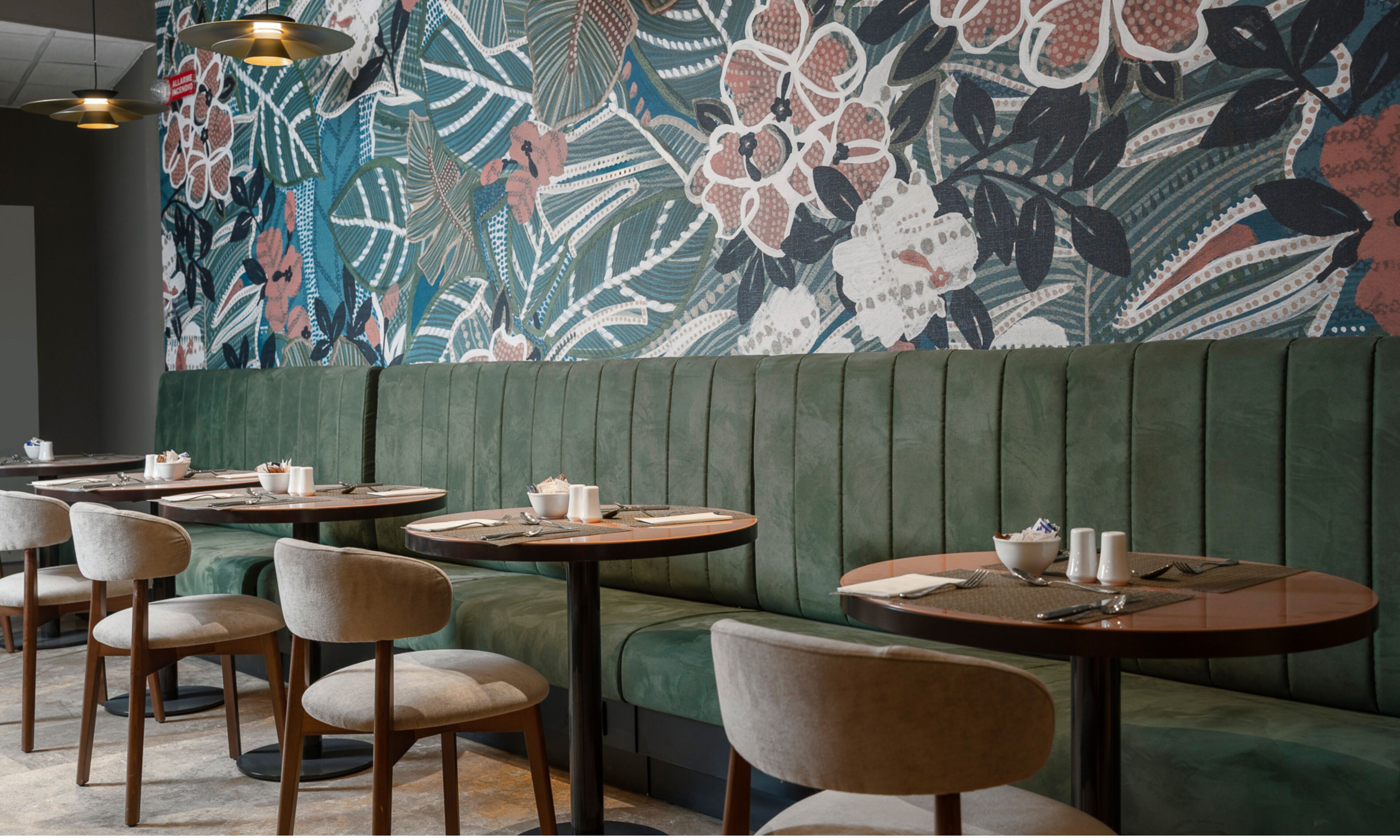 A restaurant interior with round tables, cushioned booths, and a large floral mural on the wall.