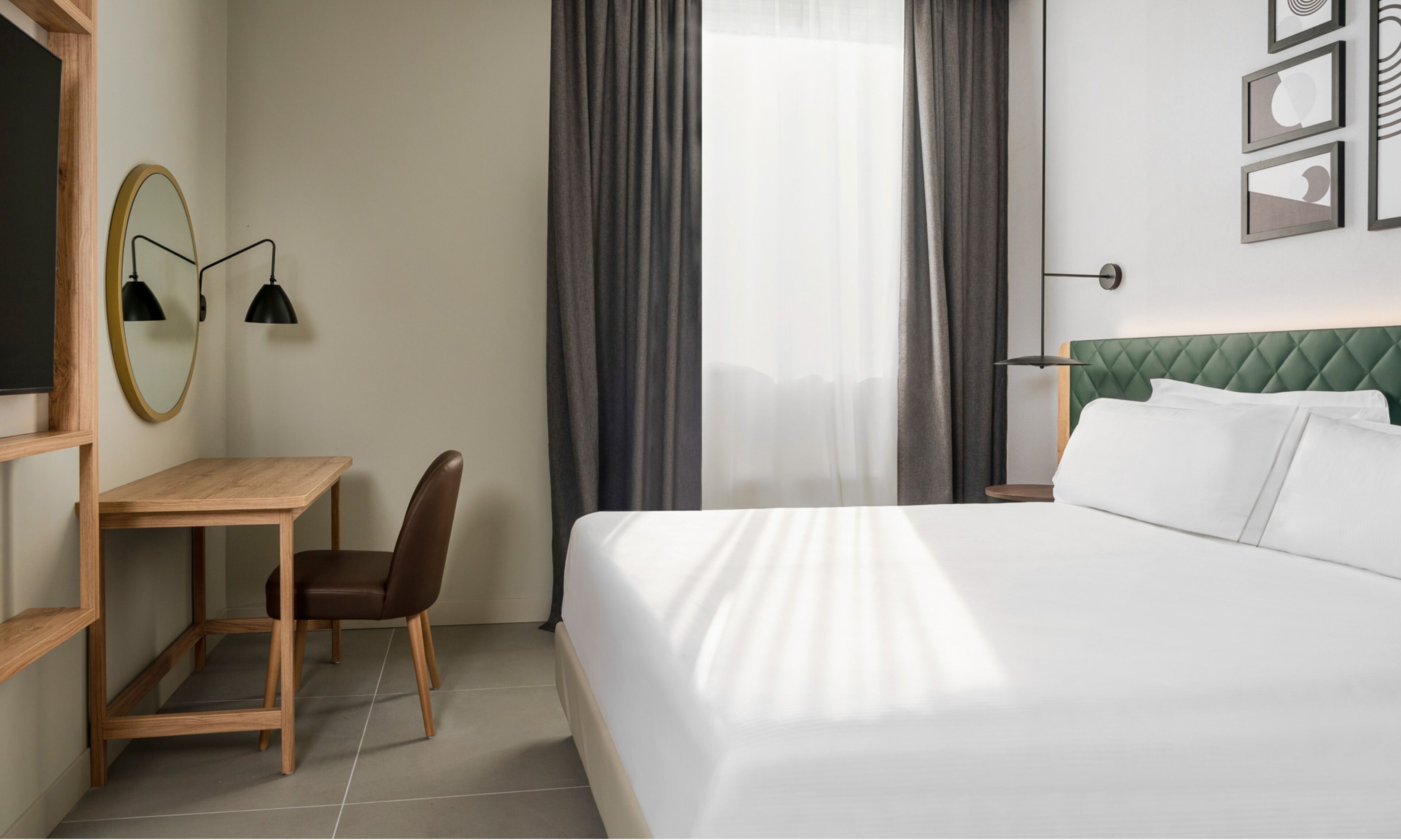 Ein Hotelzimmer mit Bett, Schreibtisch, Stuhl, Spiegel und einem Fenster mit Vorhängen.