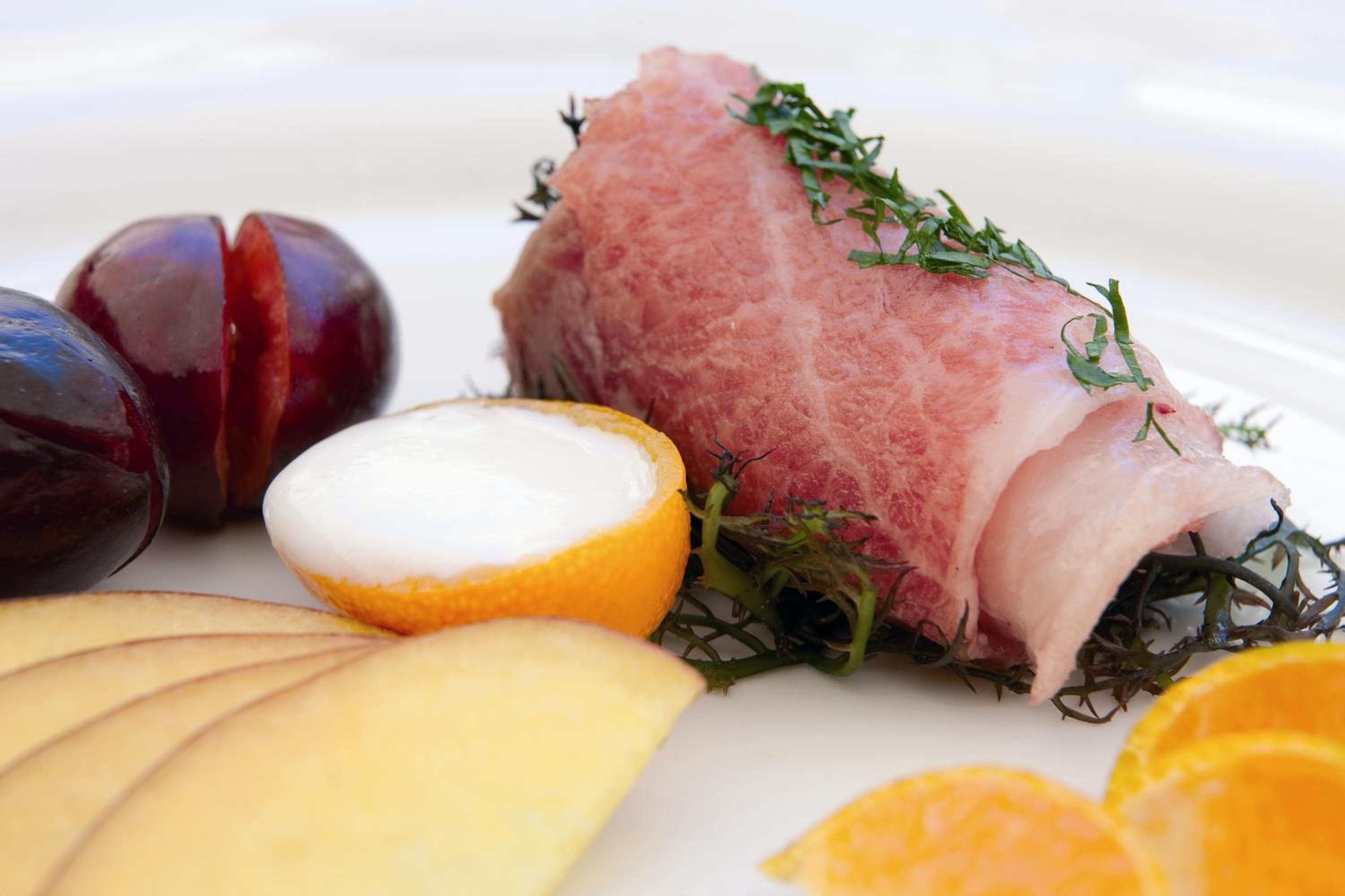 A plate with a piece of meat, a halved orange, and sliced cheese.
