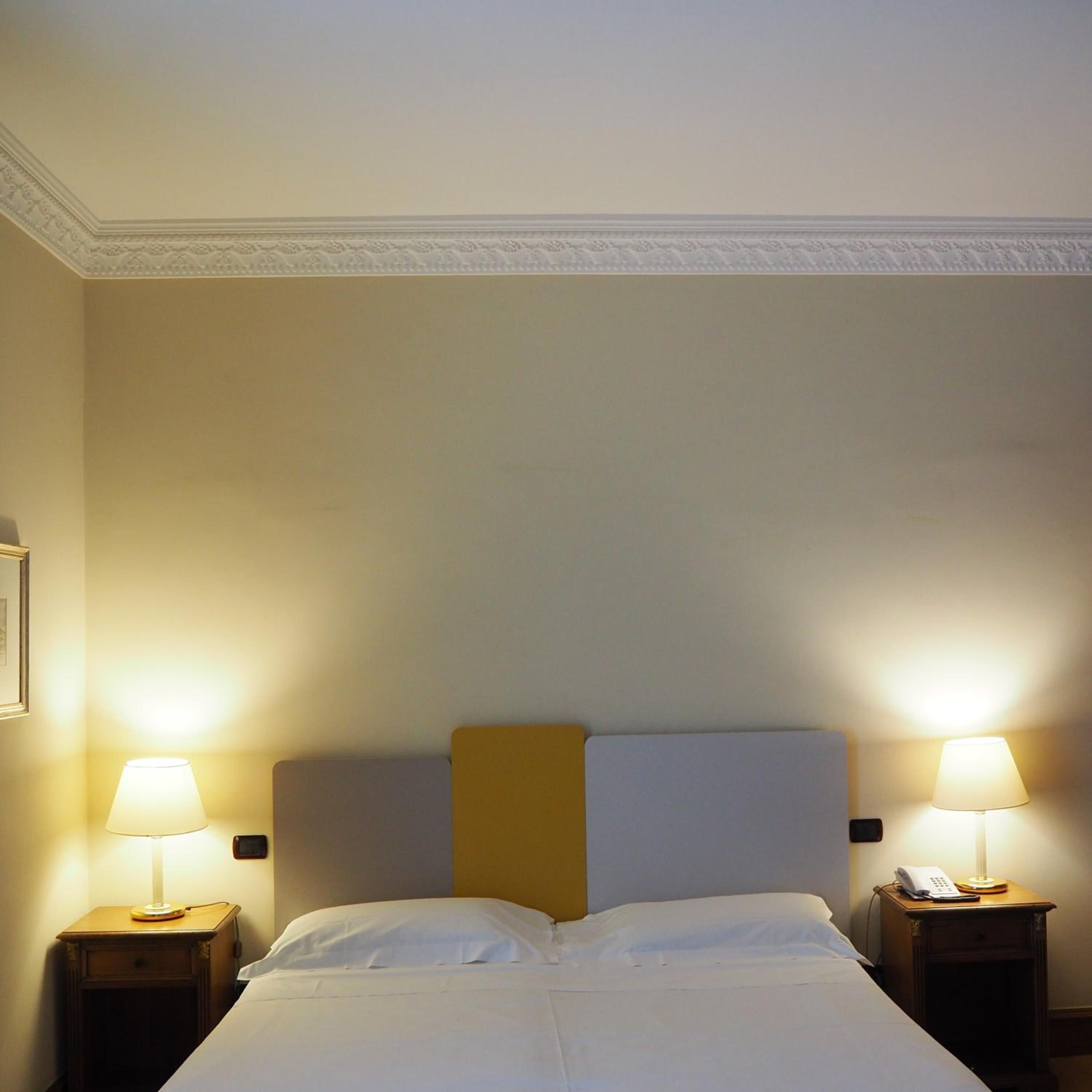 Une chambre d’hôtel avec un lit, deux tables de chevet avec des lampes et un mur uni.