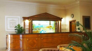 A reception area with a wooden reception desk, a large window with a view of a landscape, a clock on the wall, and a potted plant.