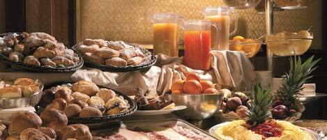 A breakfast buffet with various breads, pastries, fruits, and juices.