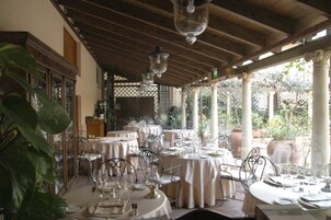 Un ristorante con tavoli e sedie rotonde, coperto da un tetto in legno e ampie finestre che si affacciano su un giardino.