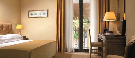 Habitación de hotel con cama, una silla, escritorio con lámpara, un cuadro en la pared y vistas por la ventana.