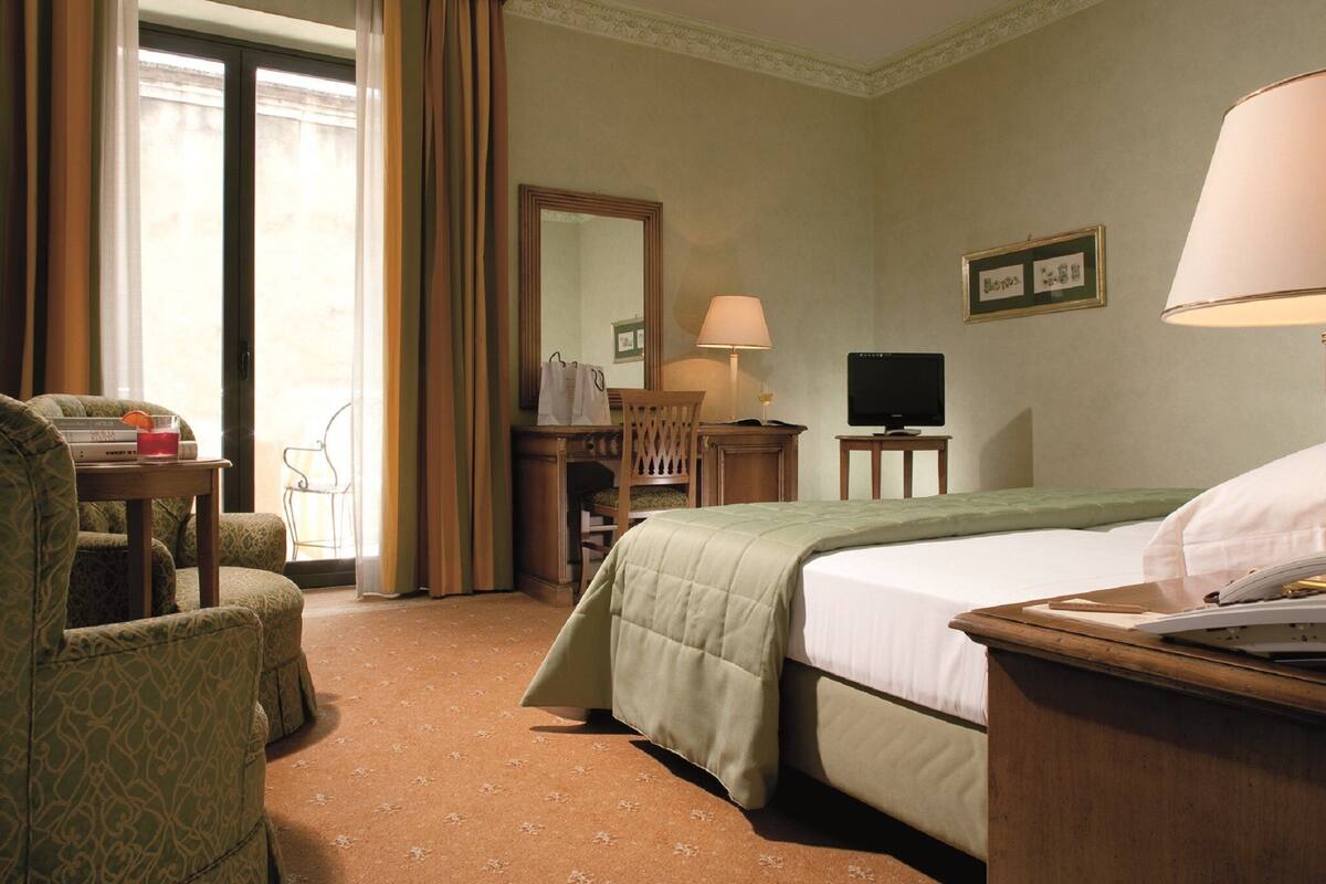 A hotel room with a bed, a desk, a chair, a television, and a window with curtains.