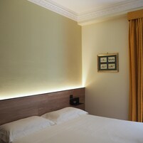 A hotel room with a bed, a headboard, a wall-mounted picture frame, and a curtain.