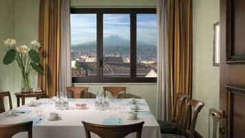 A dining room with a table set for six, a vase of flowers, and a view of a mountain through a large window.