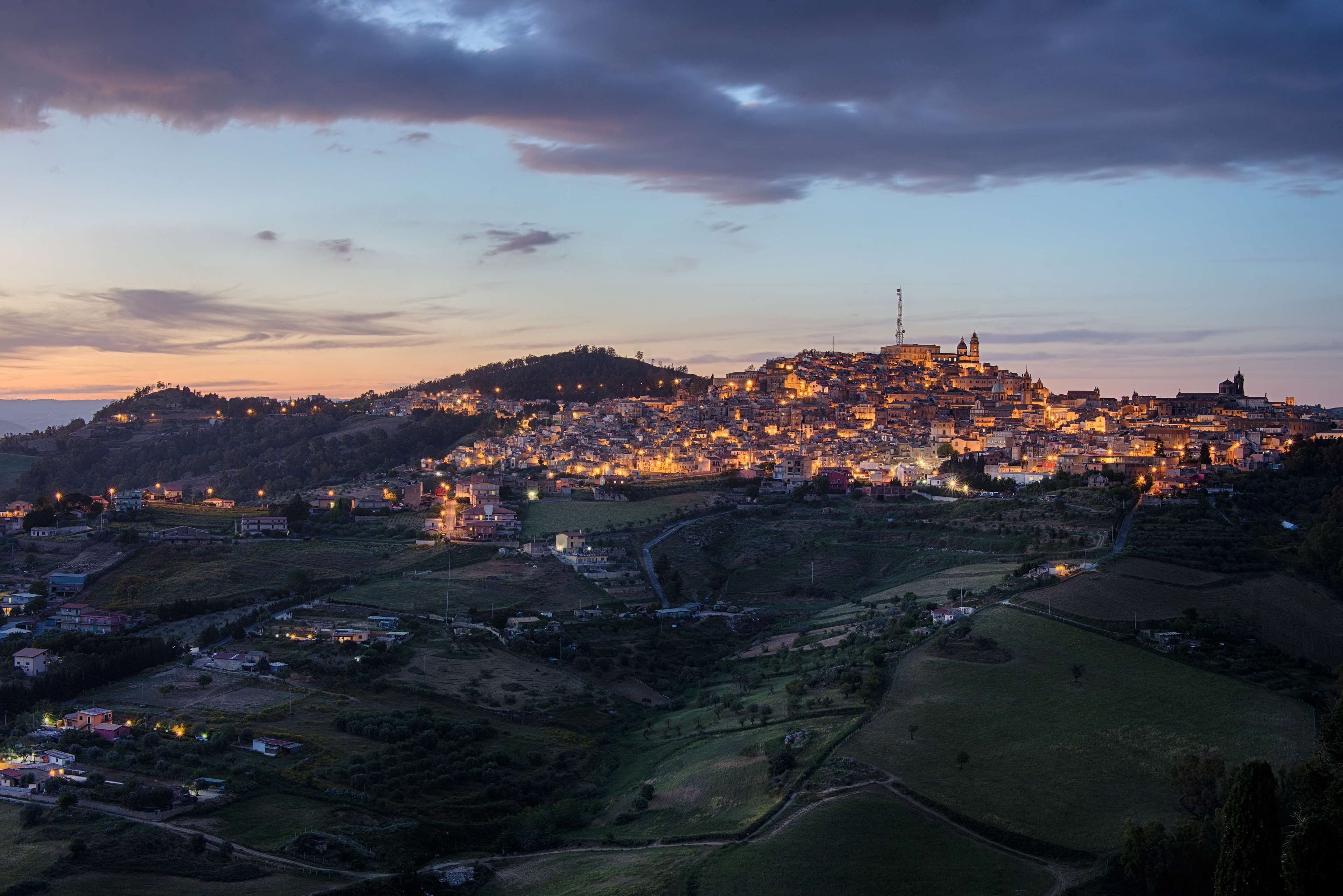 A panoramic view of a historic town with a prominent cathedral on a hill, surrounded by residential areas and fields.