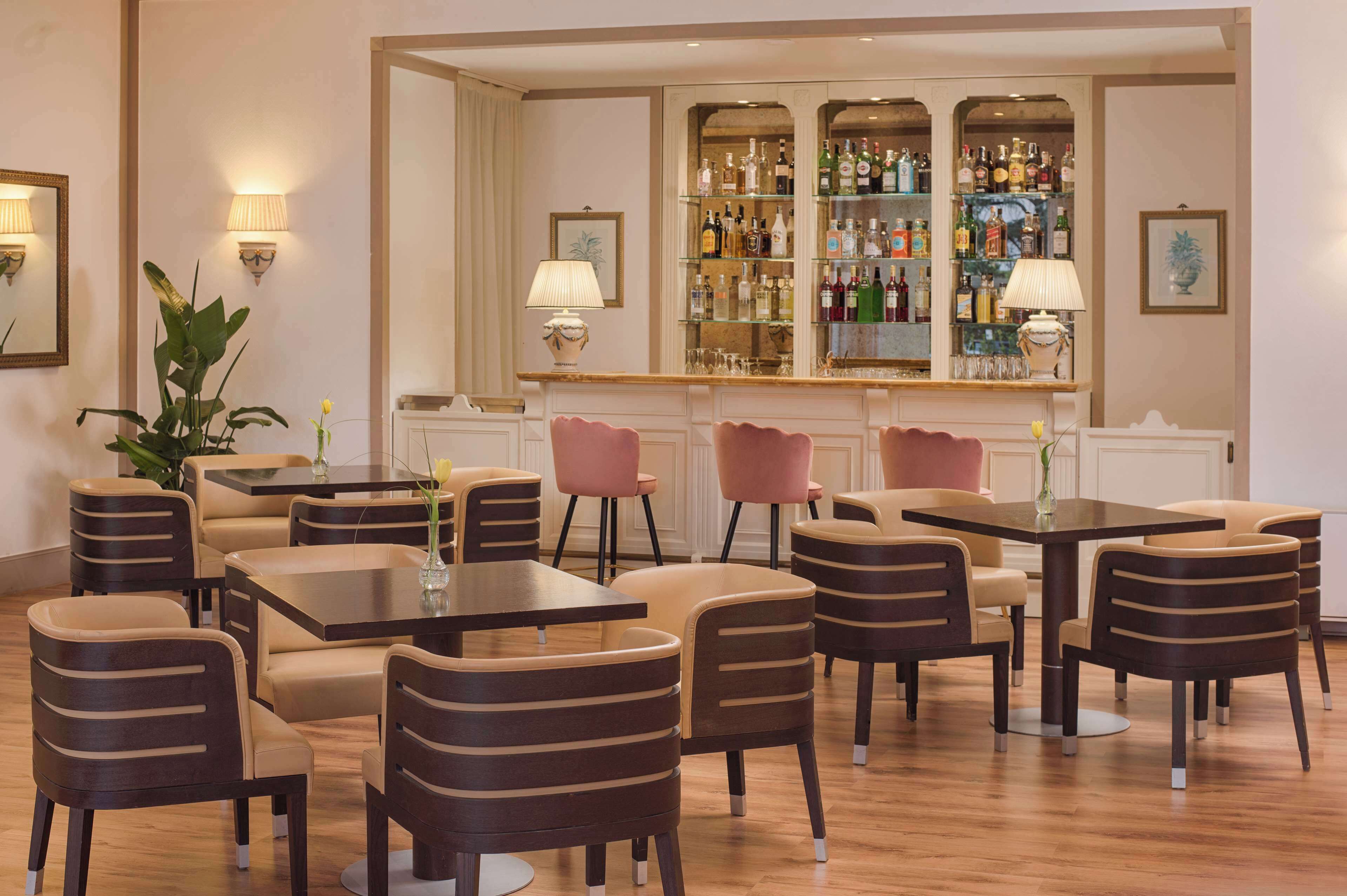 Zona de bar con varias mesas y sillas, un barral repleto de licores y apliques decorativos en la pared.