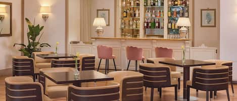 Zona de bar con varias mesas y sillas, un barral repleto de licores y apliques decorativos en la pared.