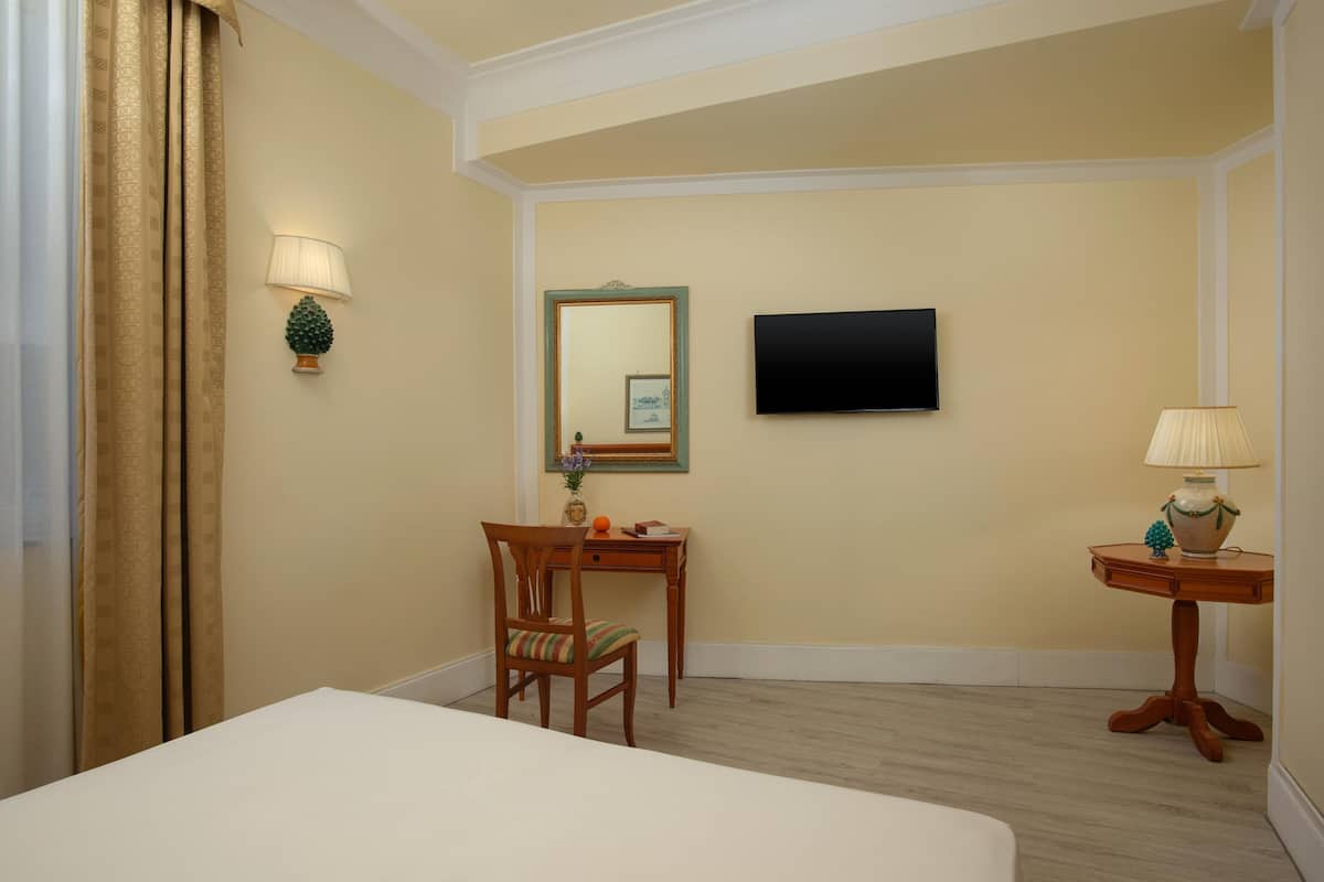Een hotelkamer met een bed, een bureau, een stoel, een televisie en een lamp.