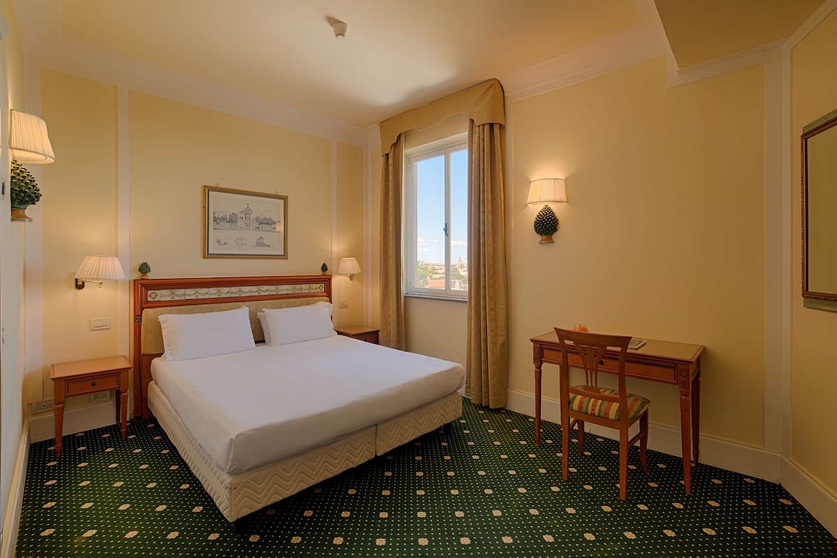 Een hotelkamer met een groot bed, een bureau, een stoel en een raam met gordijnen.