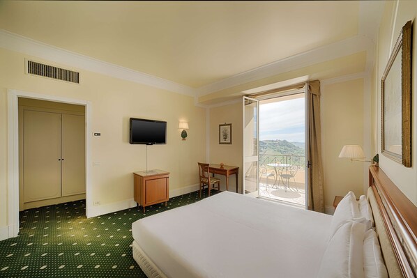 Une chambre d’hôtel équipée d’un lit, d’un bureau, d’une chaise, d’une télévision et d’un balcon avec vue.