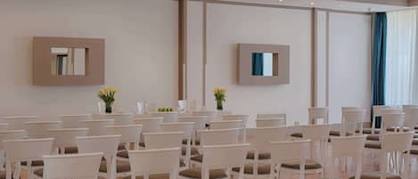 A conference room with rows of white chairs, a large table, and two wall-mounted mirrors.