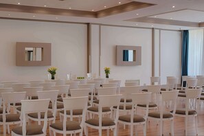 Une salle de conférence avec des rangées de chaises blanches, une grande table et deux miroirs fixés au mur.
