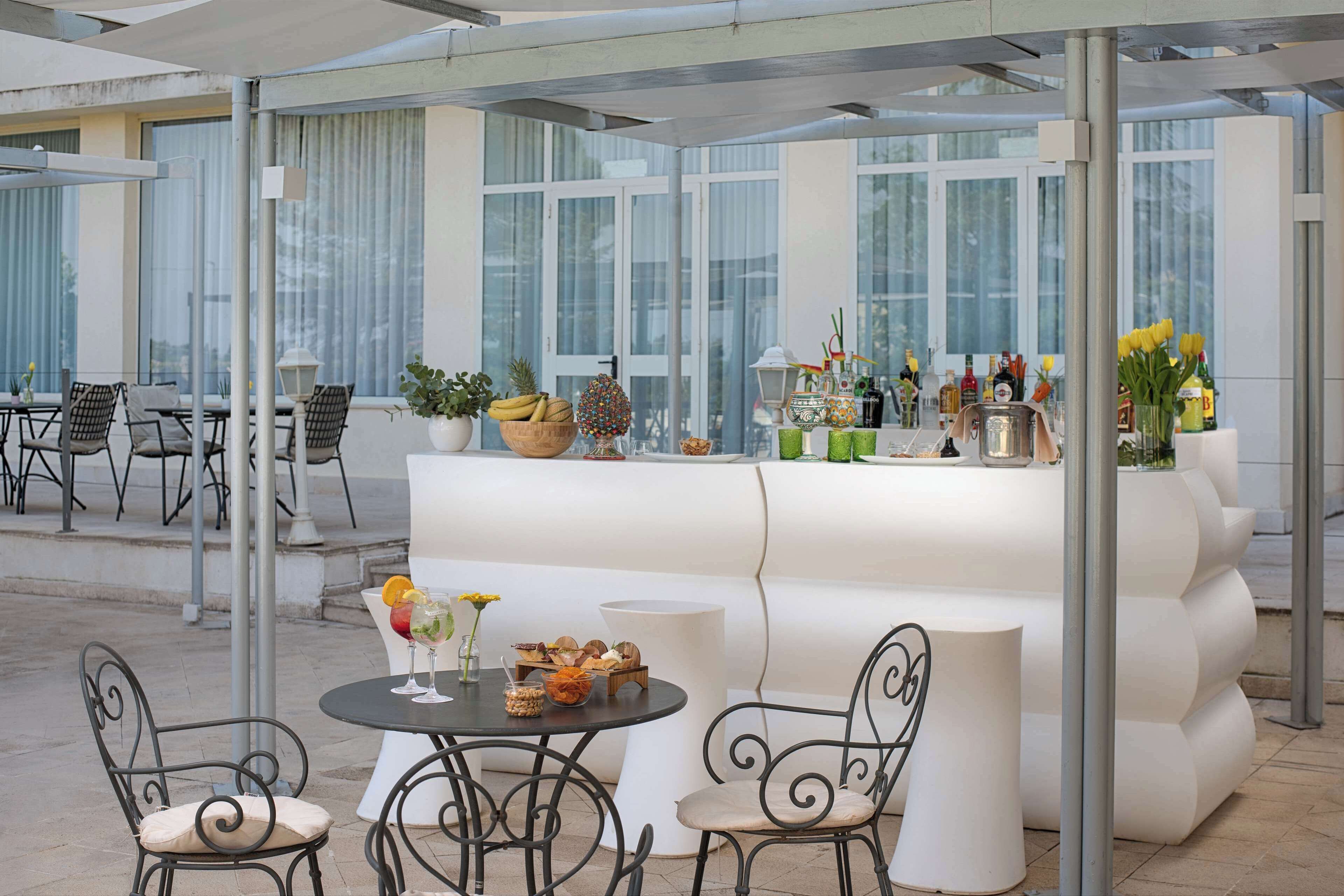 Un espace extérieur moderne, aménagé avec un comptoir de bar blanc, des chaises en métal noir et un espace clos par des parois de verre, doté de grandes fenêtres.