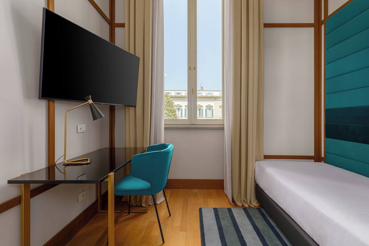 Une chambre d’hôtel moderne équipée d’une télévision à écran plat, d’un bureau avec une chaise, d’un lit et offrant une vue sur les bâtiments par la fenêtre.
