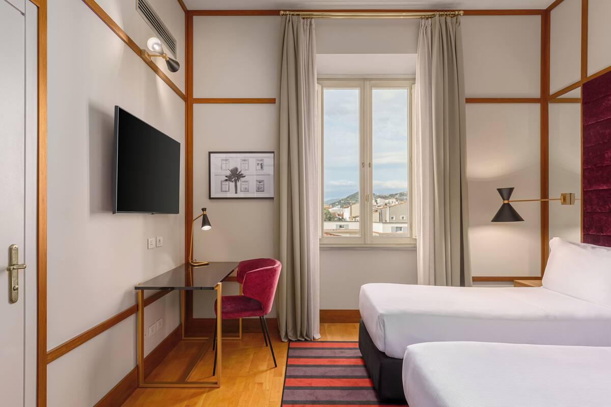 Une chambre d’hôtel équipée d’un lit, d’un bureau, d’une chaise, d’une télévision et d’une fenêtre donnant sur un paysage agréable.