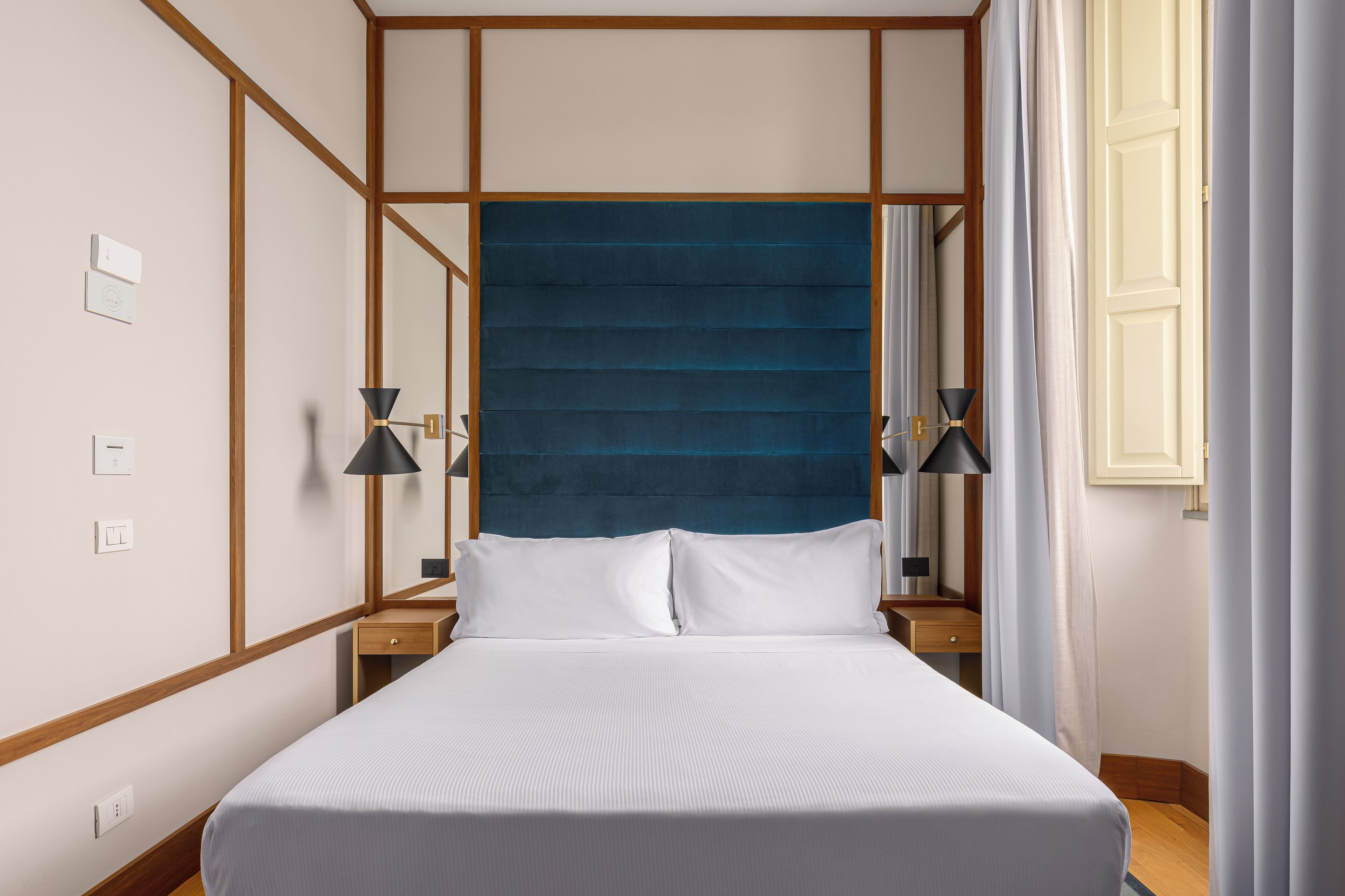 Un lit bien fait, avec du linge de lit blanc, deux tables de chevet avec des lampes, une tête de lit bleue recouverte de tissu et un plancher en bois.