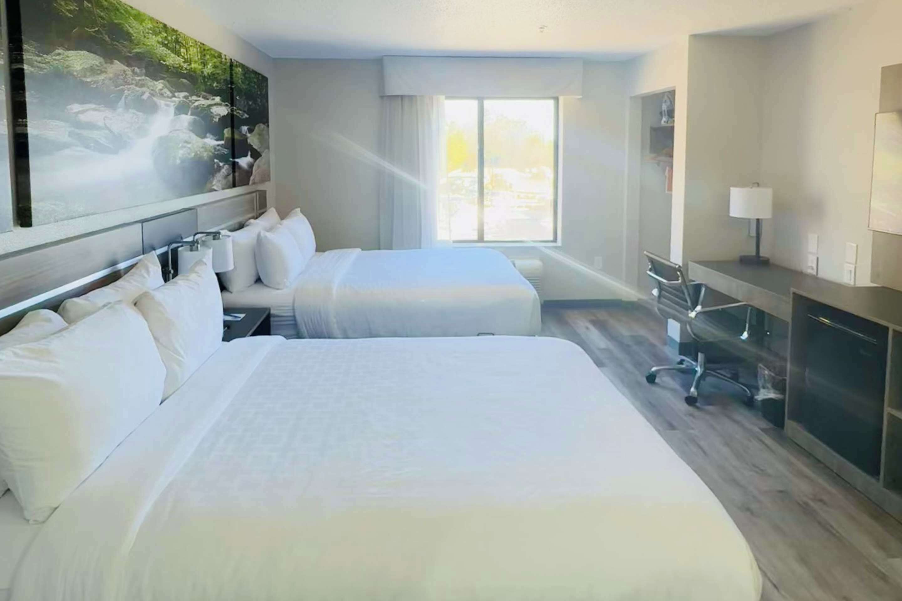 Habitación de hotel con dos camas, un escritorio, una silla y un ventanal grande.