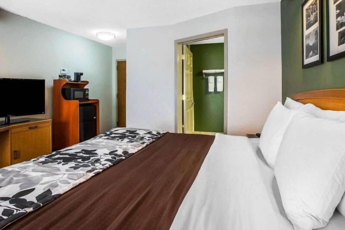 A hotel room with a bed, a TV, a microwave, and a door leading to a bathroom.