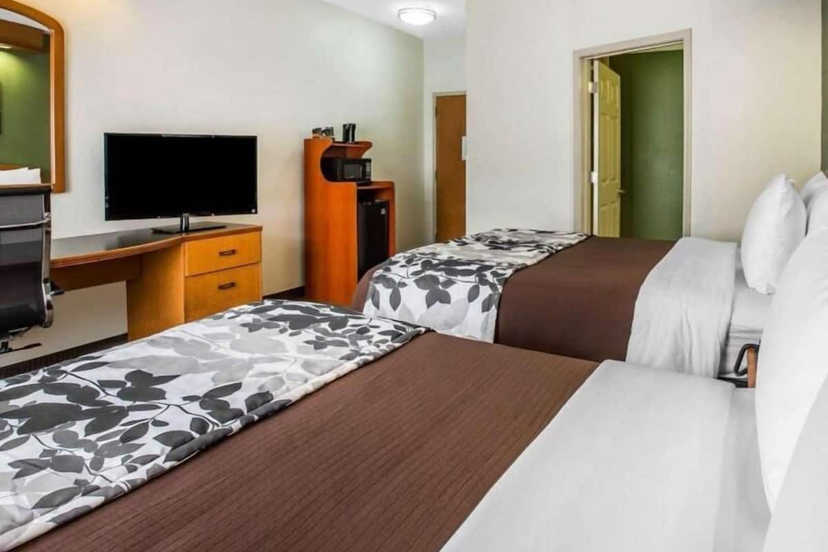 A hotel room with two beds, a desk with a television, a microwave, and a door leading to another room.